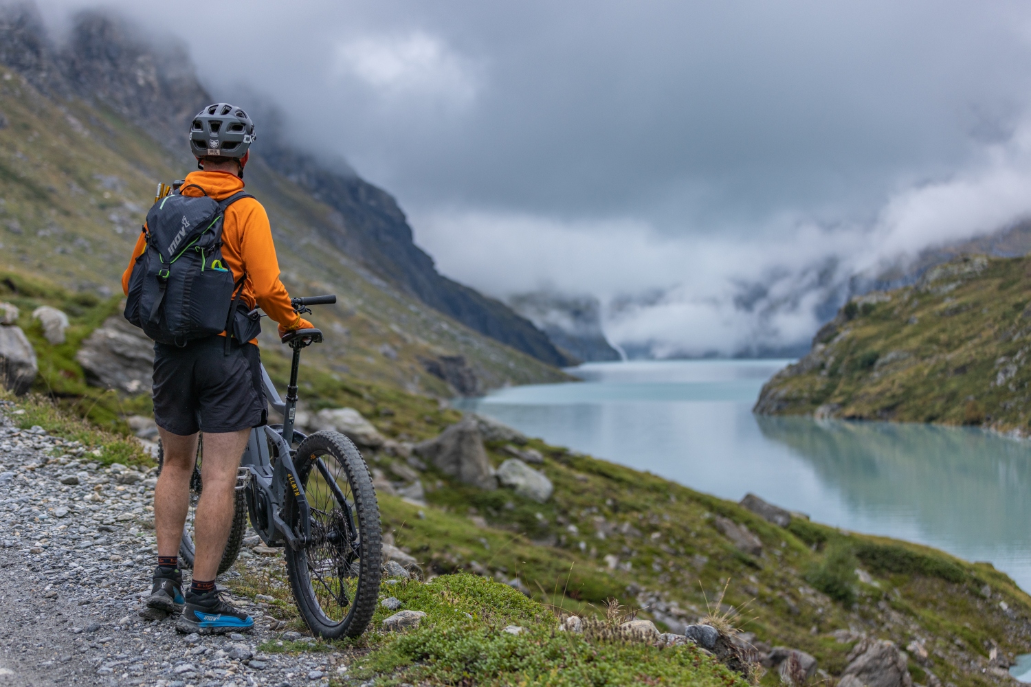 Man resting with bike looking over misty reservoir - Verbier